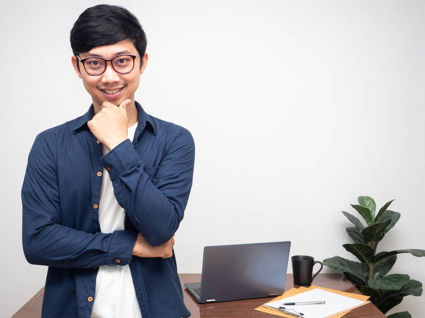 Jovem empresário vestindo óculos cruz braço e gesto pensando em negócios com sala de trabalho - Foto, Imagem