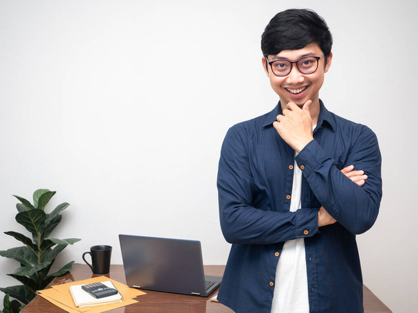 Homme d'affaires positif portant des lunettes croix bras et geste penser à l'entreprise avec salle de travail - Photo, image