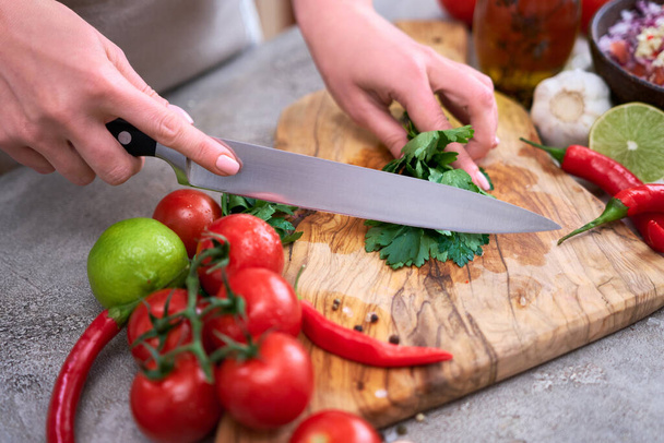 making salsa dip sauce - woman cutting and chopping cilantro or parsley on wooden cutting board. - Fotoğraf, Görsel