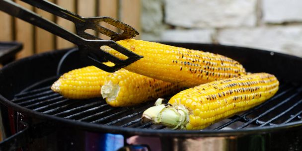 Tourner le maïs sur la grille de l'épi sur la grille arrière-cour avec une fourchette en acier poignées. - Photo, image