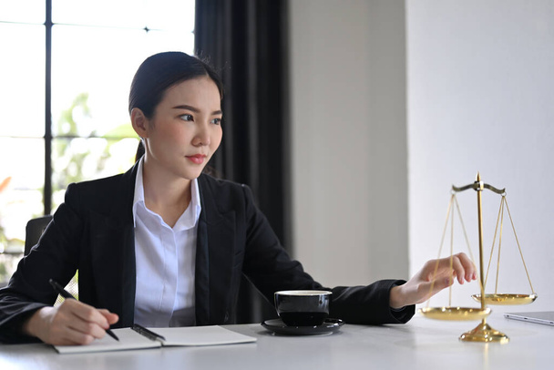 Abogada de negocios asiática profesional y confiada o justicia se sienta en su escritorio de la oficina, mirando por la ventana. Derecho y concepto jurídico - Foto, imagen