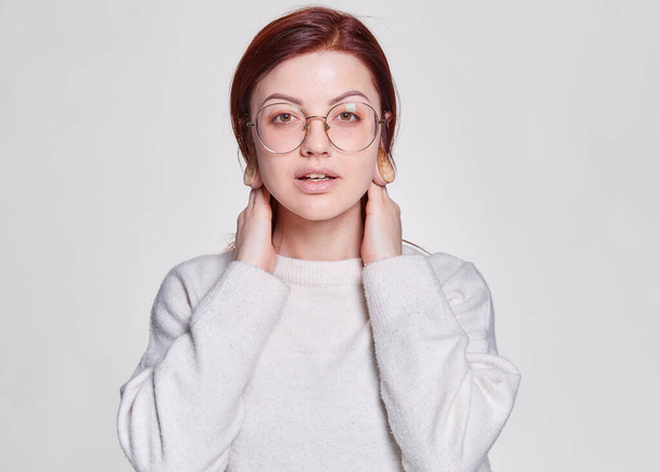 Smiling redhead woman in big eyeglasses with pierced tunnel in ears posing over white background copy space - Fotografie, Obrázek