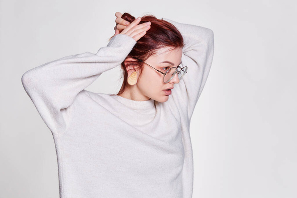 Smiling redhead woman in big eyeglasses with pierced tunnel in ears posing over white background copy space - 写真・画像