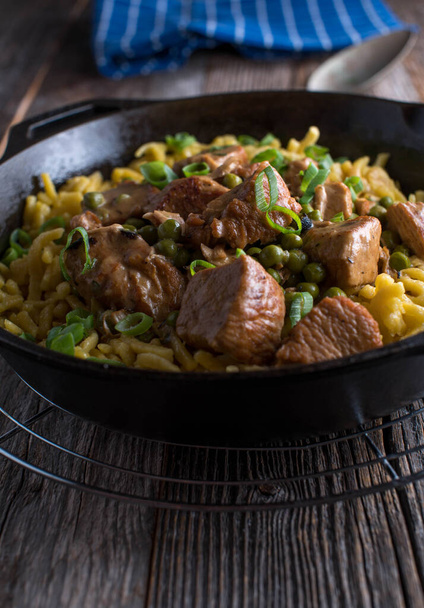 Turkey ragout with peas and egg noodles. Served in a cast iron pan on wooden table. - Photo, Image