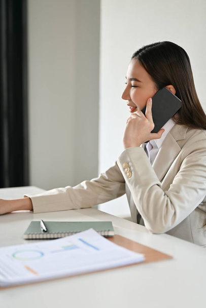Elegante mujer de negocios asiática o gerente ejecutiva en traje formal hablando por teléfono con su equipo en la oficina. - Foto, Imagen