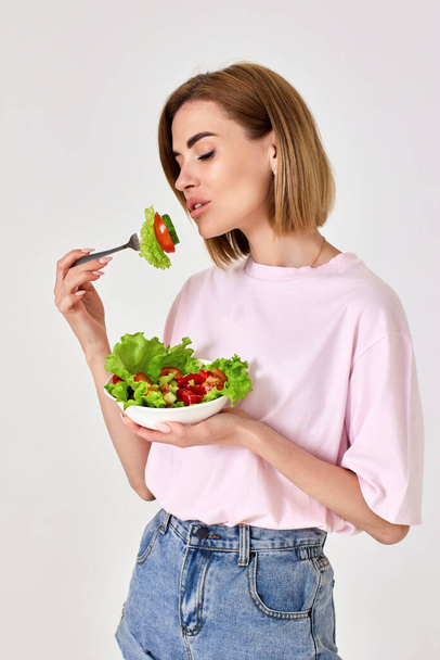 beautiful smiling blonde woman eating fresh vegetable salad on white background - Photo, image