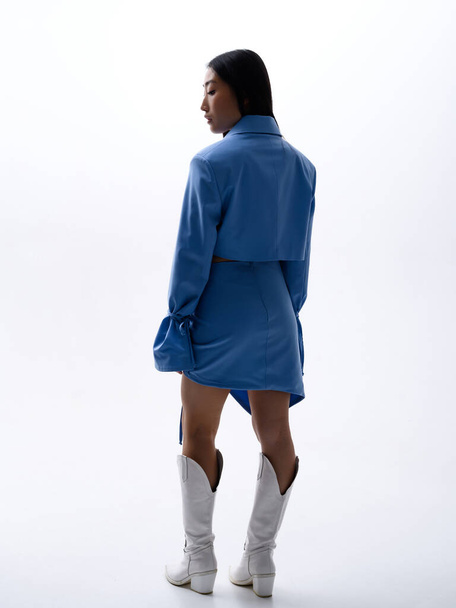 Una hermosa chica asiática en un traje azul posa contra una pared blanca en un estudio fotográfico - Foto, imagen