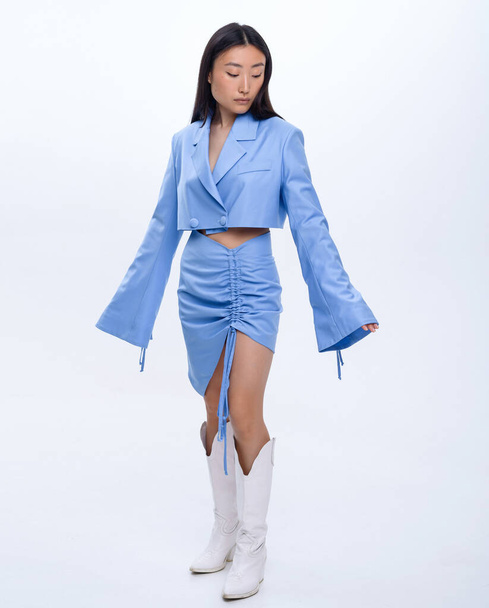 A beautiful Asian girl in a blue suit poses against a white wall in a photo studio - Foto, Imagen