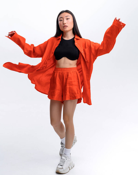 Belle fille asiatique en lin orange costume décontracté posant contre le mur blanc dans le studio photo - Photo, image