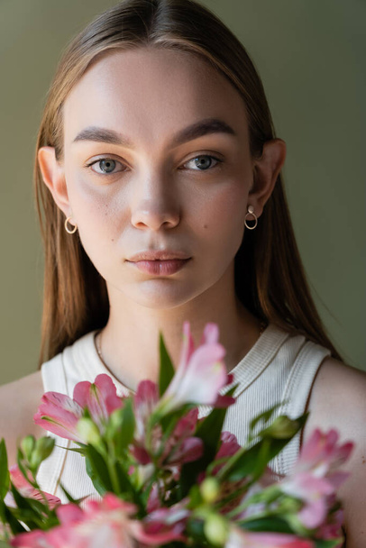 portrait of woman with natural makeup near blurred alstroemeria flowers isolated on green - Фото, зображення