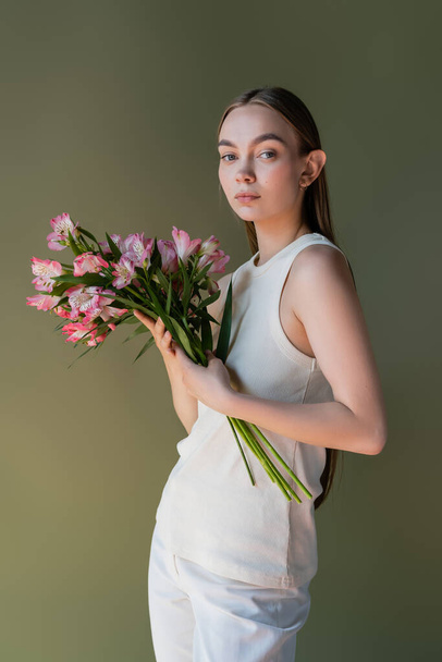 long haired woman posing with pink alstroemeria flowers isolated on green - 写真・画像
