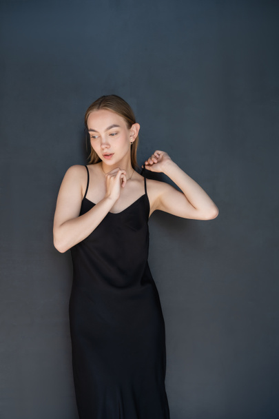 sensual woman touching strap of black dress on dark background - Photo, Image