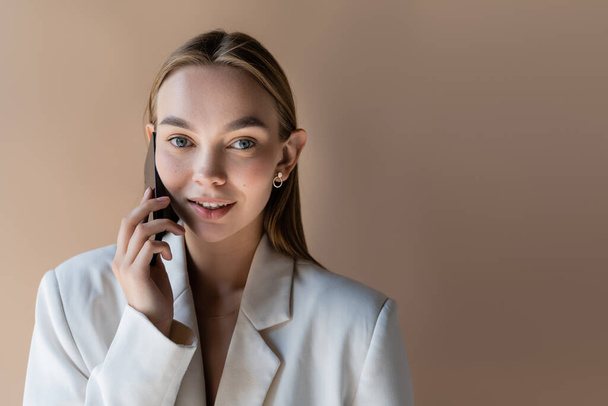 smiling and stylish woman talking on mobile phone isolated on beige - Fotografie, Obrázek