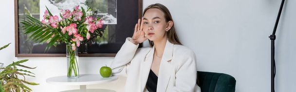 femme à la mode regardant la caméra près de pomme mûre et bouquet sur la table basse, bannière - Photo, image
