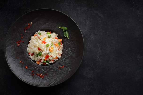Risotto with vegetables and spices on a black plate, on a black background - Foto, afbeelding