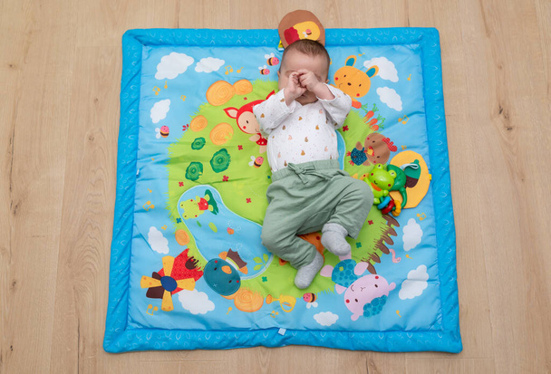 Baby girl lying on a blue play mat while is playing with her hands. Montessori activities. - Fotoğraf, Görsel