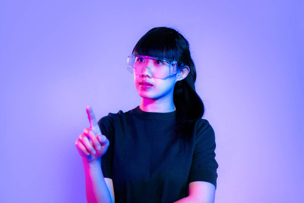 Metaverse concept. Young asian woman in black t-shirt wearing vr classes posing touching on purple neon light color background. - Photo, Image