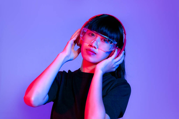 Young asian girl in black t-shirt wearing glasses and red headphones posing on purple color background. - Foto, Imagem