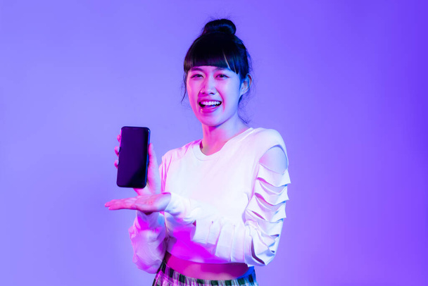 Young asian woman in white fashion sweatshirt using and holding and showing black screen smartphone on the purple background. - Photo, Image