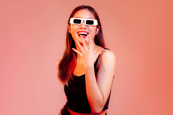 Young asian woman long hair in black tank top wearing sunglasses posing happy and surprised on red screen background - Foto, immagini