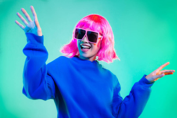 Young asian woman in blue sweatshirt pink short hair punk style wearing sunglasses posing dancing on the green screen background. - 写真・画像