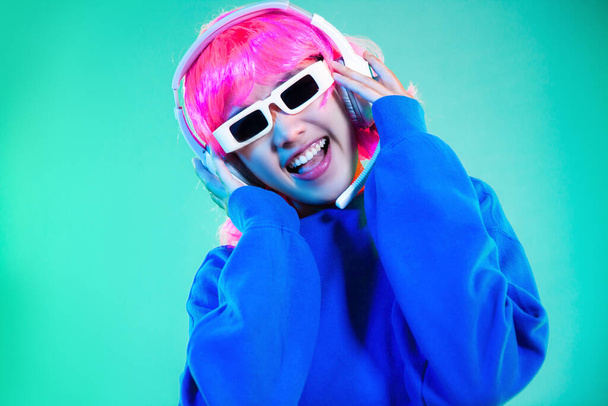 Young asian girl pink color hair punk style in blue sweatshirt wearing sunglasses and headphone on green screen background.	 - Foto, immagini