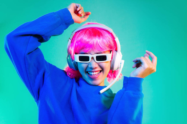 happy asian woman in blue sweatshirt pink short hair punk style wearing sunglasses and headphones dancing on the green background.	 - Foto, Imagen