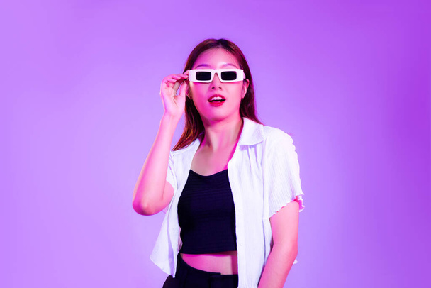 młoda Azji kobieta w czarny zbiornik top i biały koszula noszenie okulary przeciwsłoneczne pozowanie na fioletowy tło.. - Zdjęcie, obraz