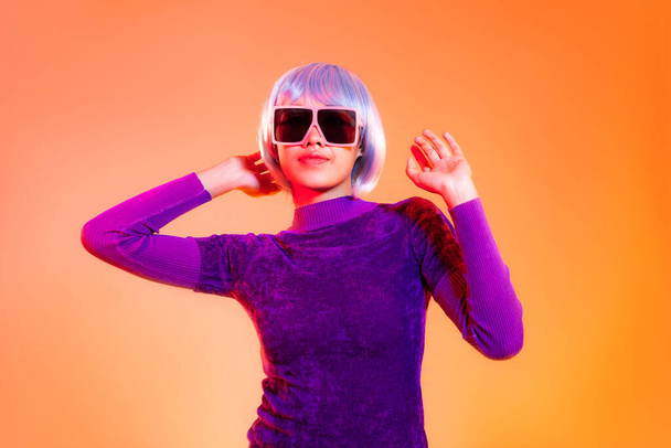 Metaverse concept. Young asian girl in purple shirt wearing sunglasses posing on the orange screen background. - Φωτογραφία, εικόνα