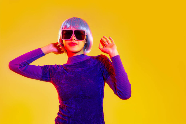 Cyber punk girl concept, asian woman in purple sweatshirt silver and blue short hair style wearing sunglasses posing like robot islated yellow background. - Foto, immagini