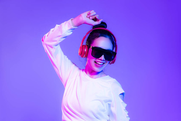 Young asian woman in white crop shirt wearing sunglasses and red headphone dancing on the purple background. - Valokuva, kuva