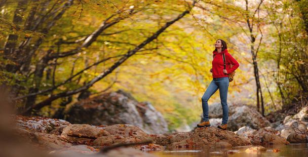 Sonbaharda seyahat ve yolculuk konsepti. Macera ve aktif yaşam tarzı. Ormanda turist yürüyüşü. Kırmızı kapüşonlu Asyalı kadın ormanda yürüyor. Seyahat tutkusu konsepti. - Fotoğraf, Görsel