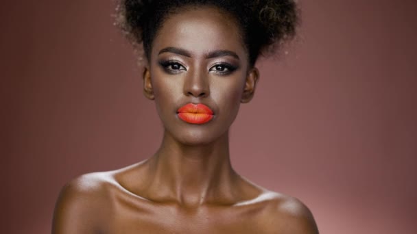 Серьёзная африканская американка с красочным макияжем, смотрящая в камеру на коричневом фоне - Кадры, видео
