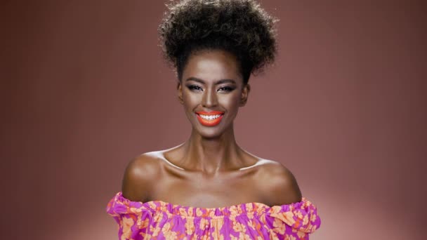 Усміхнена африканська етнічна молода жінка з барвистим модним макіяжем, дивлячись на камеру, ізольована на коричневому фоні
 - Кадри, відео