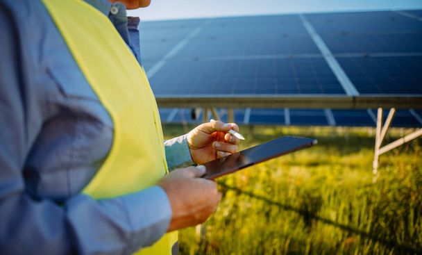 Alternative source of electricity. Inspector engineer man holding digital tablet working in solar panels power farm, photovoltaic cell park. Innovation and green power concept  - Fotoğraf, Görsel