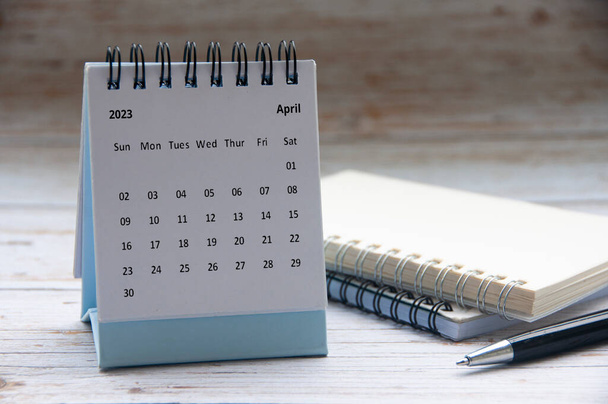 April 2023 weißer Schreibtischkalender auf Holztisch mit Notizblock und Stifthintergrund. Neujahrskonzept und Kopierraum - Foto, Bild