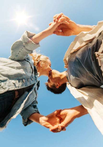 summer holidays, love and people concept - happy young couple kissing under blue sky, from below - Fotó, kép
