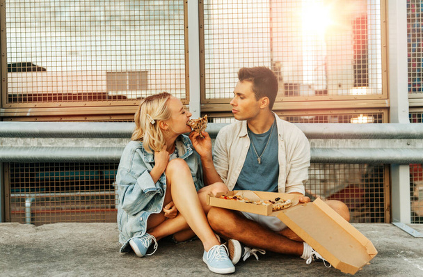 summer holidays, food and people concept - happy young couple eating takeaway pizza on city roof top parking - 写真・画像
