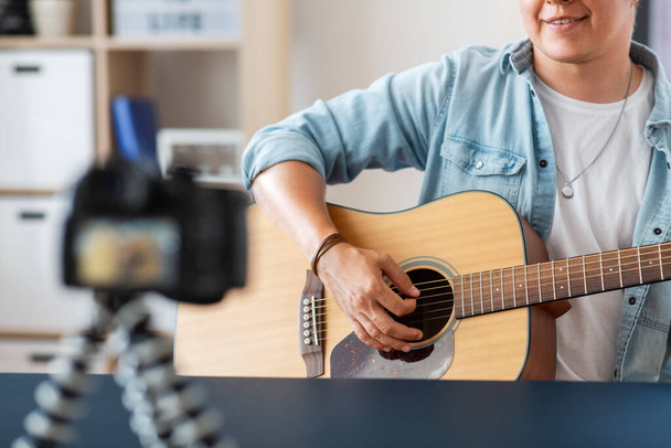 music, blogging and people concept - close up of male guitarist or musician with camera playing acoustic guitar and recording video or live streaming at home - Photo, image