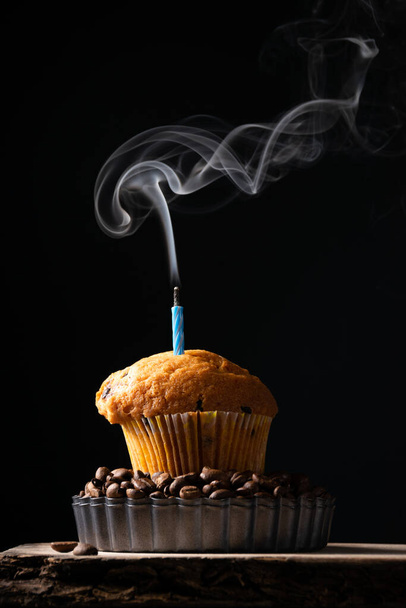 A coffee muffin with smoking candle on dark background, festive background, baking themes - Photo, image