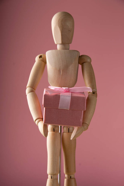 Close up of wooden mannequin holds a pink gift box - Fotografie, Obrázek