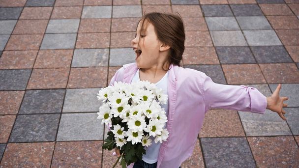 high angle view of amazed kid with outstretched hand holding flowers outside - Foto, Imagen