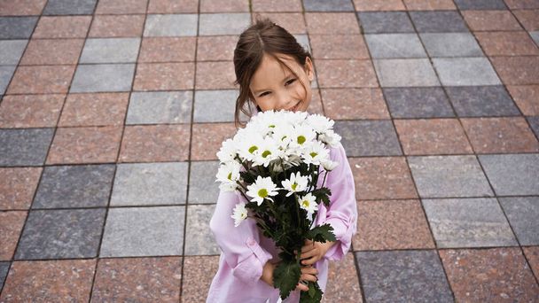 high angle view of happy kid holding bouquet of while flowers outside - Foto, imagen