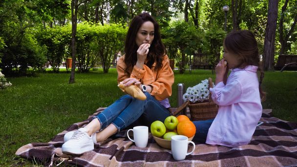 mother and child eating fresh baguette during picnic in park - Fotoğraf, Görsel