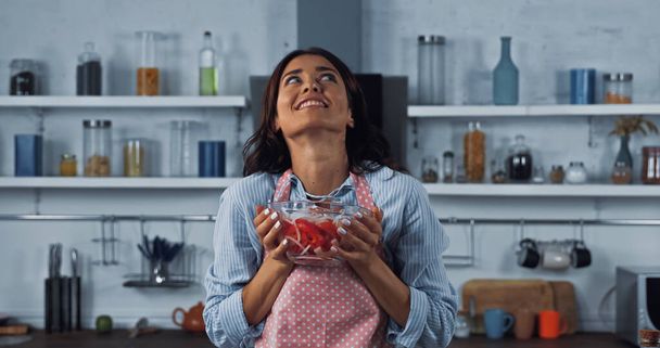 excited woman with bowl of fresh vegetable salad looking up in kitchen - Fotó, kép