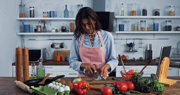 brunetka hospodyňky krájení syrové cibule v blízkosti různých zeleniny a vajec na kuchyňském stole - Fotografie, Obrázek