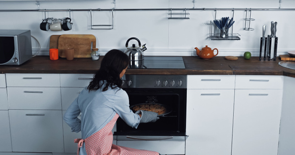 brunette woman baking sweet pie in electric oven at home - Foto, afbeelding