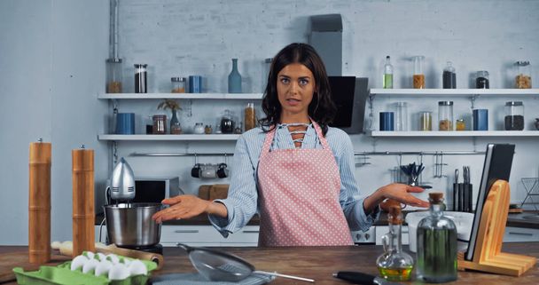 culinary vlogger pointing at ingredients and cooking utensils while looking at camera - Photo, Image