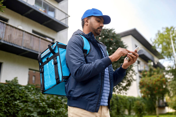 food shipping, profession and people concept - indian delivery man with thermal insulated bag and smartphone on city street - Fotoğraf, Görsel