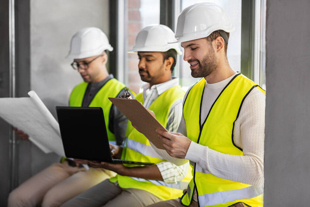 architecture, construction business and people concept - group of male architects in helmets with laptop, blueprint and clipboard working at office - Foto, Imagen